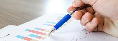 Person pointing a pen at printed graphs on a desk